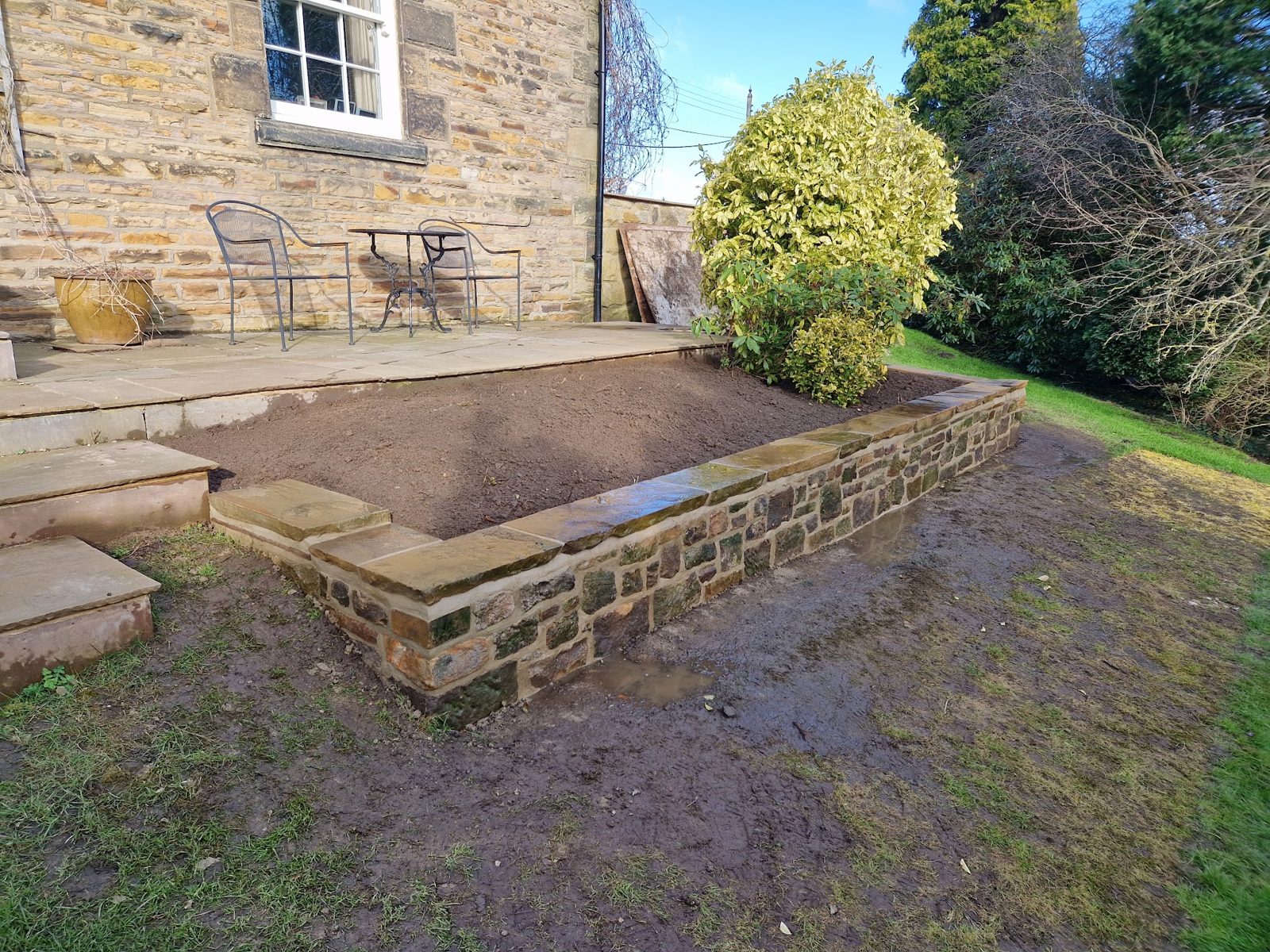 A raised bed with a new stone retaining wall beside a stone cottage patio