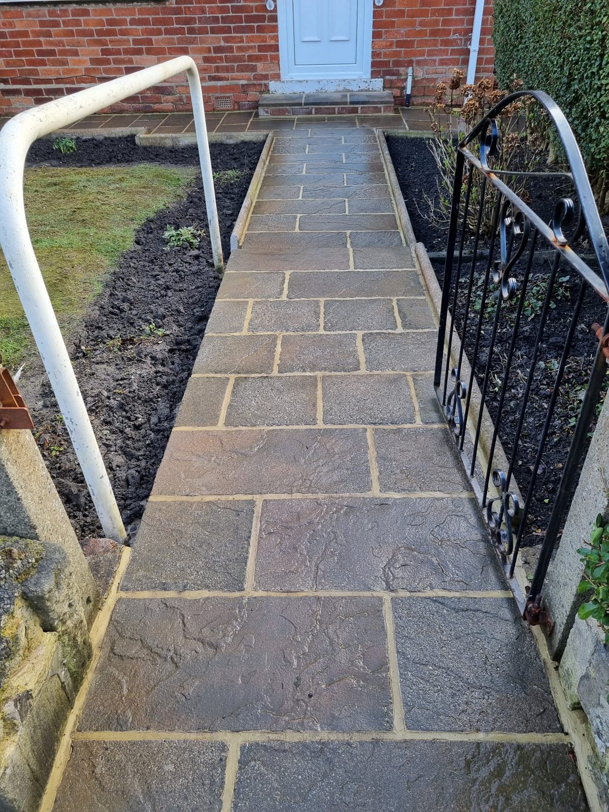 A new grey paved front path running to the door, beside a black iron gate