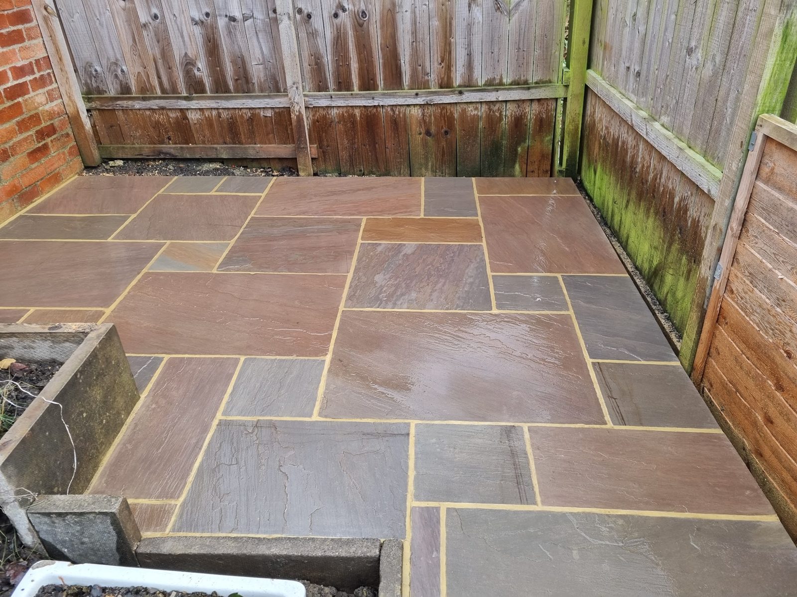 A newly laid sandstone patio with fence panels behind