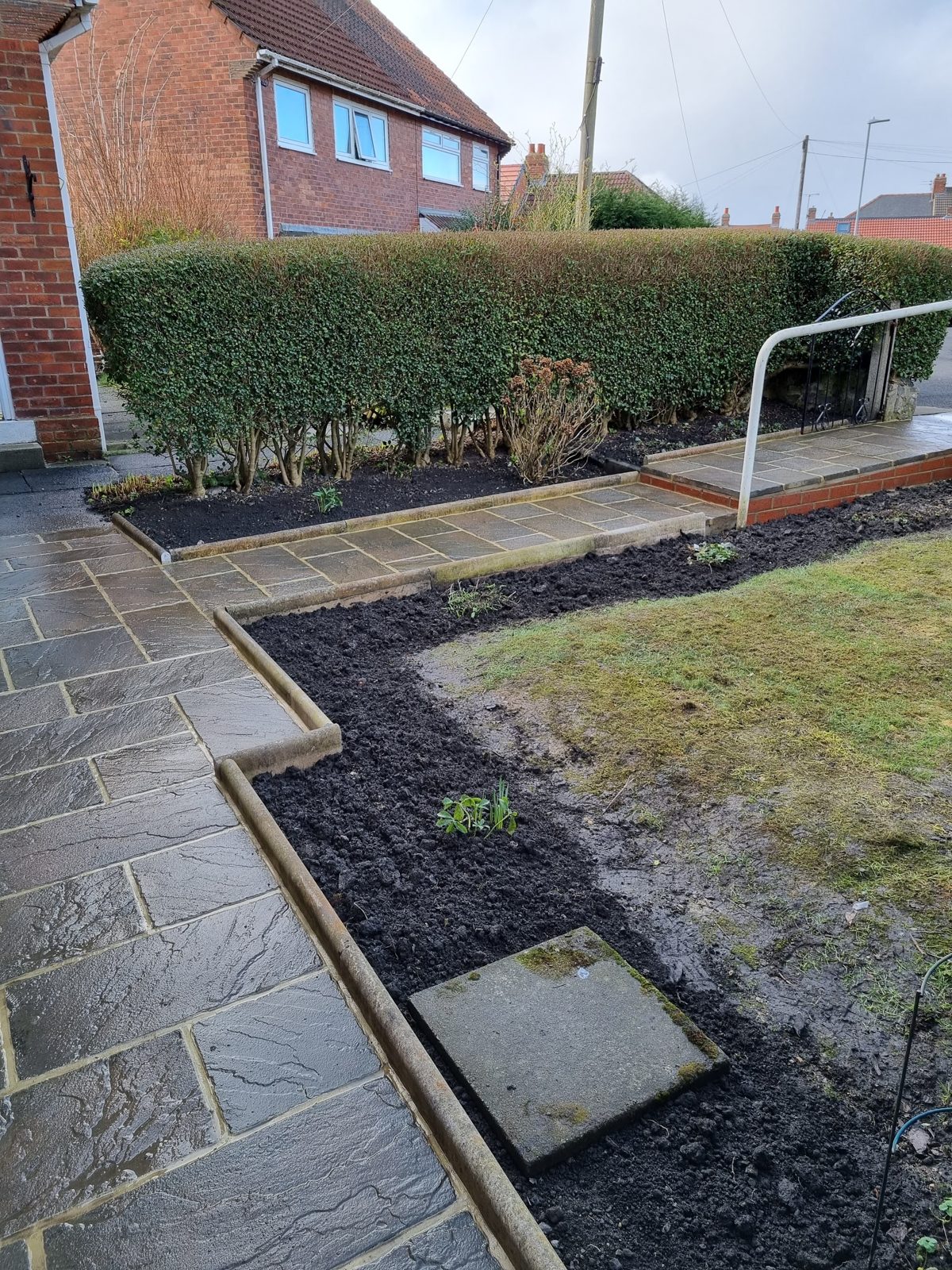 A paved path beside a freshly edged border and trimmed hedge